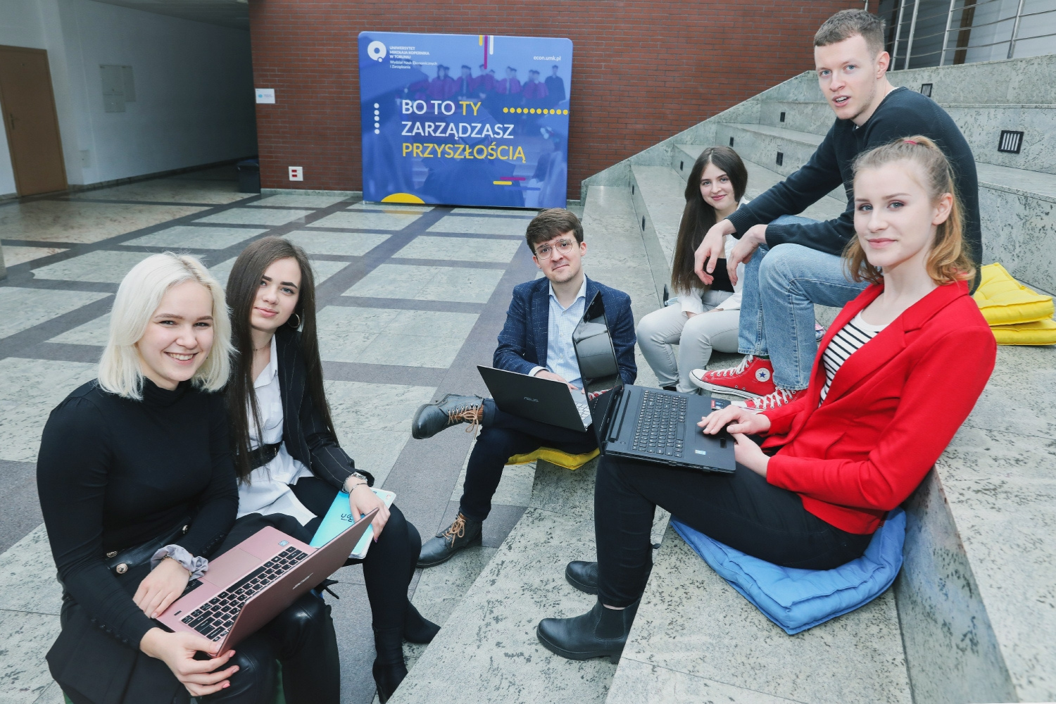 Grupa studentów pracuje przy laptopach w przestrzeni wspólnej wydziału.