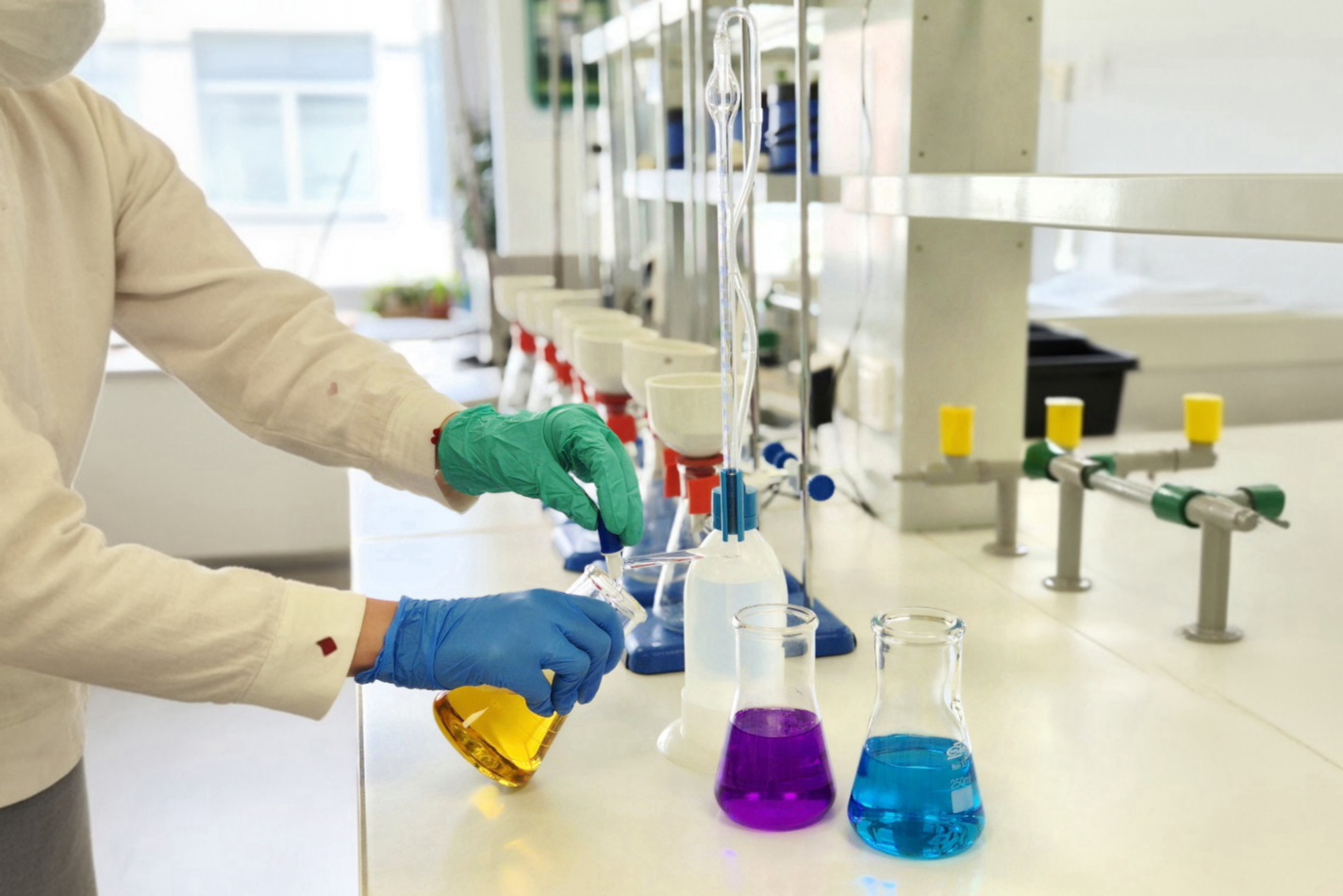 Osoba w rękawiczkach laboratoryjnych wykonuje miareczkowanie roztworu podczas zajęć laboratoryjnych.