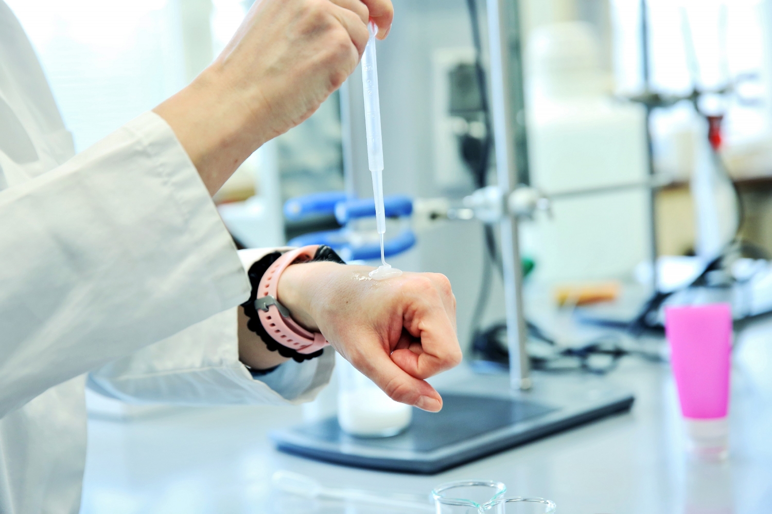 Osoba w laboratorium nanosi próbkę kosmetyczną na skórę dłoni za pomocą pipety.