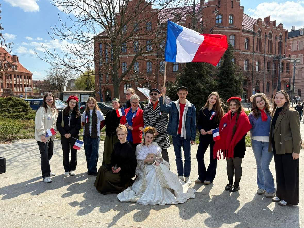 Grupa studentów i wykładowców pozuje do zdjęcia, trzymając francuską flagę i małe chorągiewki Francji.