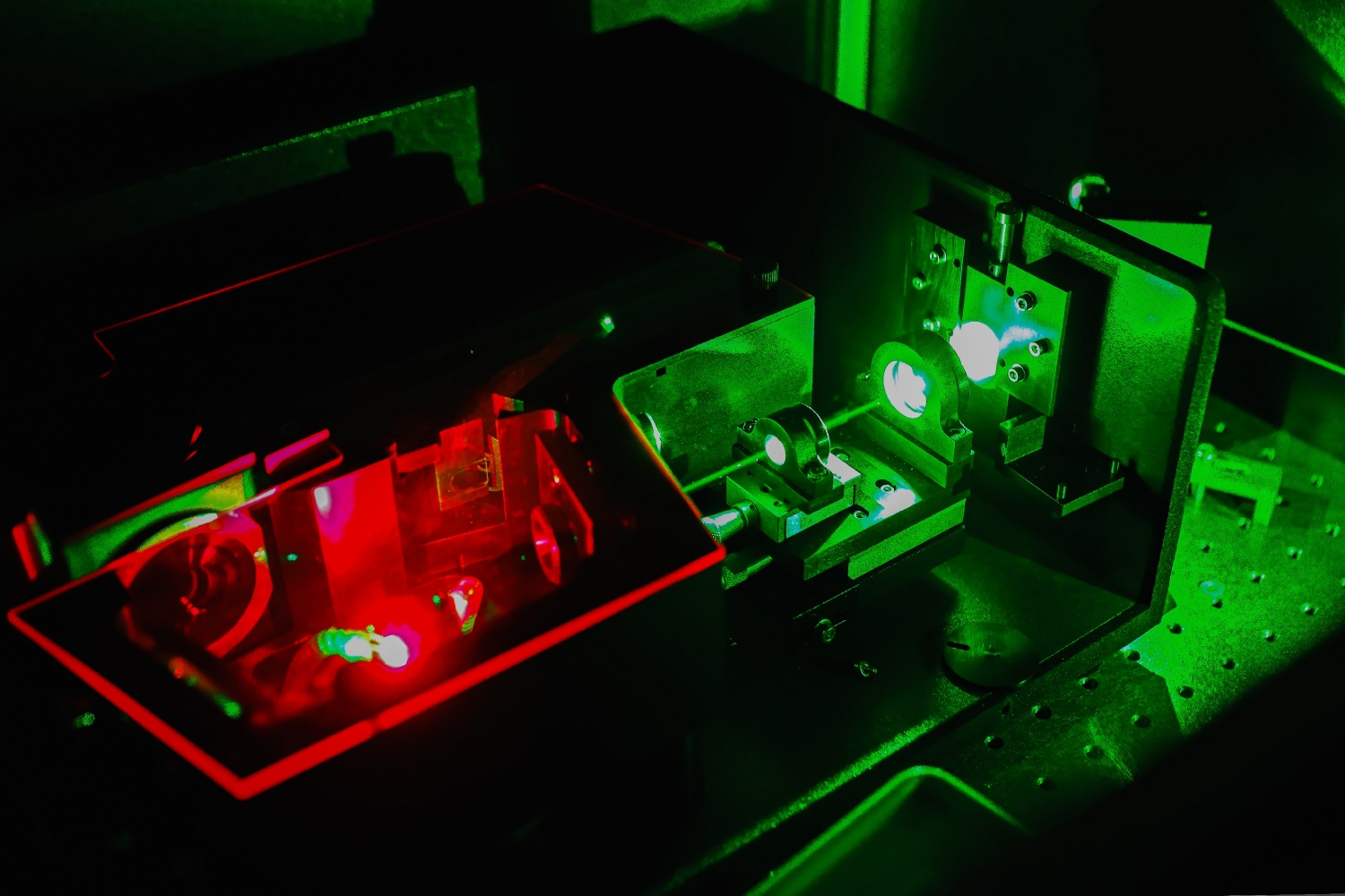 Wnęka optyczna oscylatora parametrycznego w laboratorium FAMO (Fizyki Atomowej, Molekularnej i Optycznej) Uniwersytetu Mikołaja Kopernika w Toruniu. Widoczne dwie sekcje zawierające soczewki i elementy optyczne: prawa strona oświetlona jest zieloną wiązką pompującą, a lewa strona przez czerwone światło generowane przez kryształ nieliniowy umieszczony w zamkniętej komorze. Zdjęcie wykonane w zaciemnionym pomieszczeniu laboratoryjnym.