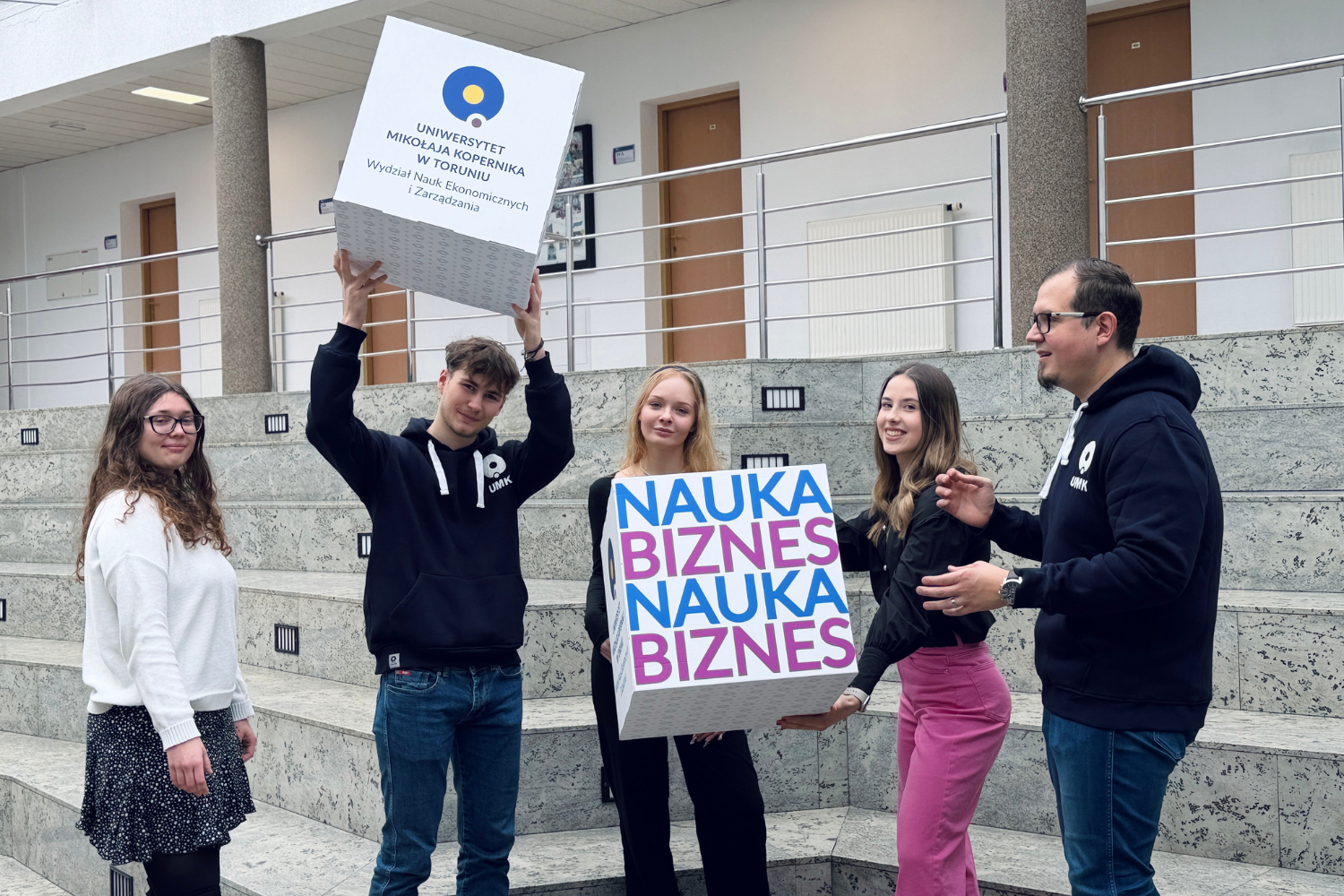 Grupa studentów prezentuje kostki promocyjne związane z ofertą studiów na wydziale ekonomicznym.